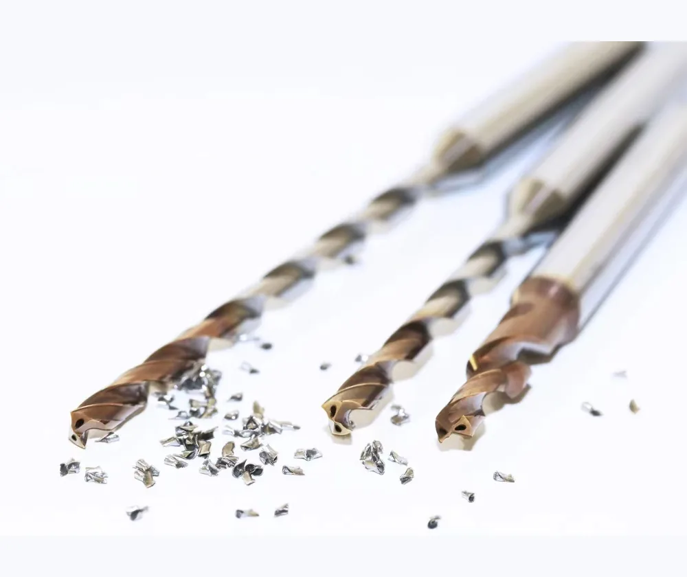 Bronze-coated solid carbide drills with coolant holes at the tips and metal chips on a white surface